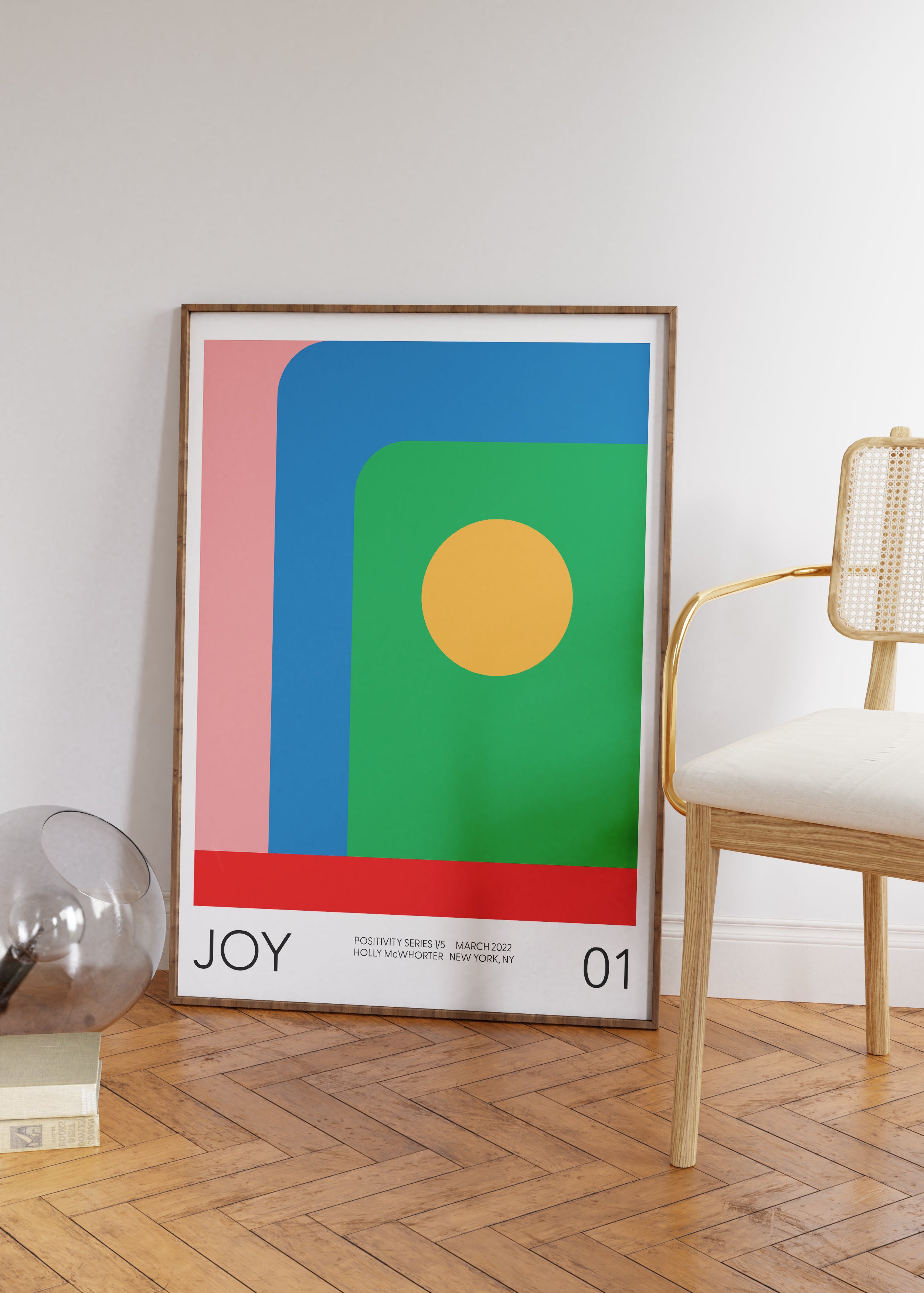 Framed abstract art print with geometric shapes and 'JOY' text in a room with a chair and decor items.